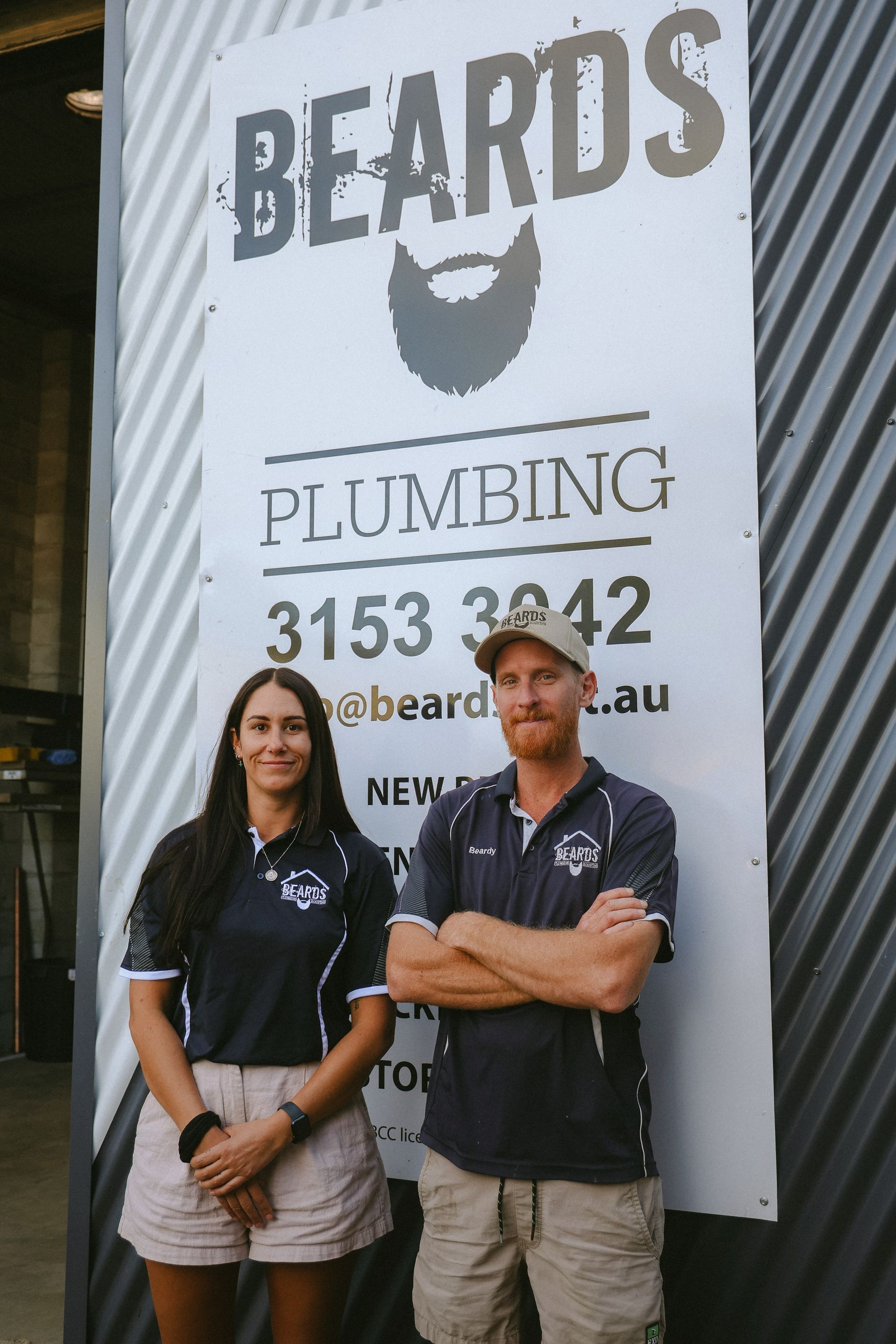 A Man And Woman Standing In Front Of A Poster On A Wall — Beards Roofing and Plumbing in Clontarf, QLD