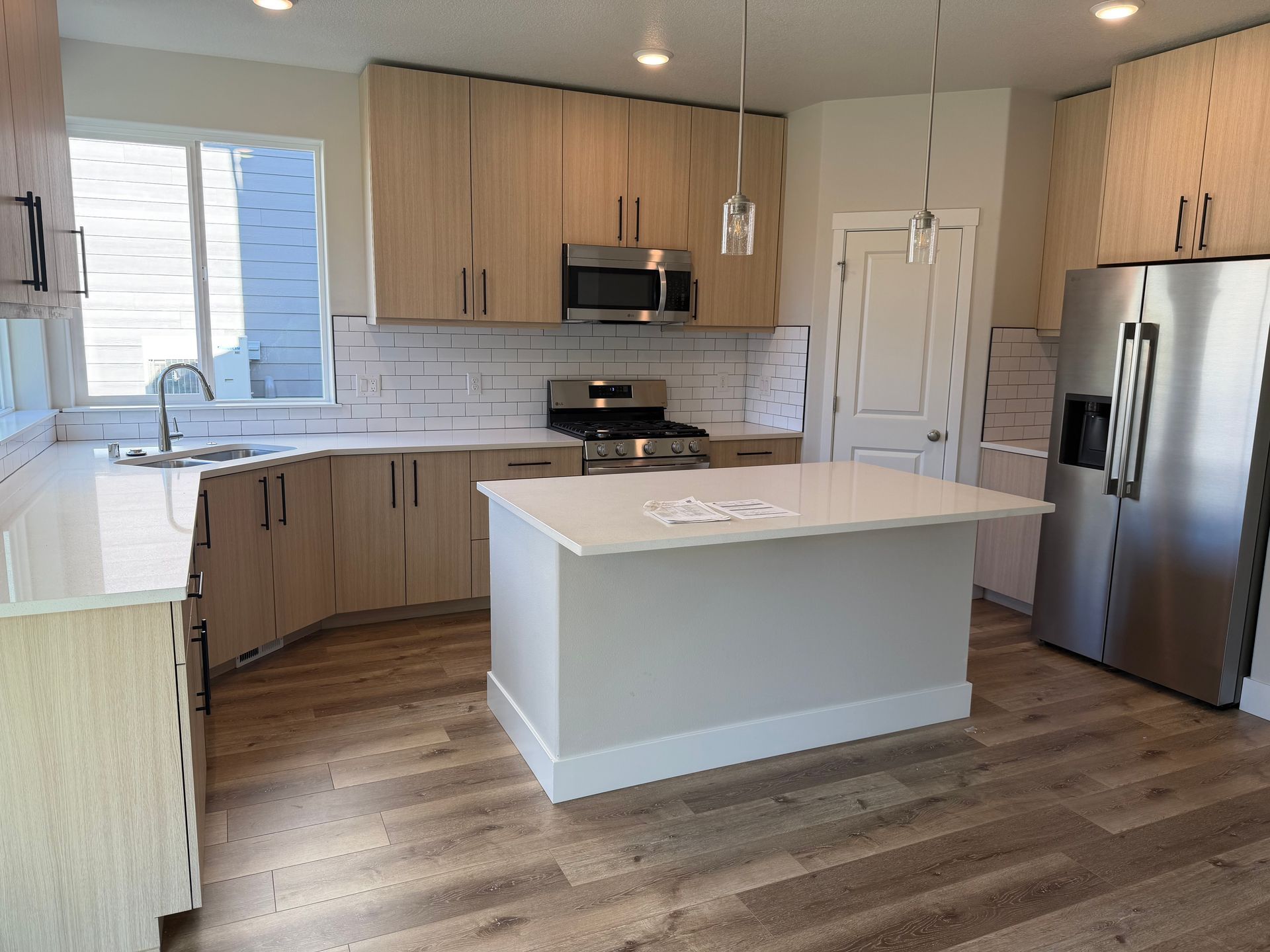 Modern kitchen with light wood cabinets, white countertops, stainless steel appliances, and an island.