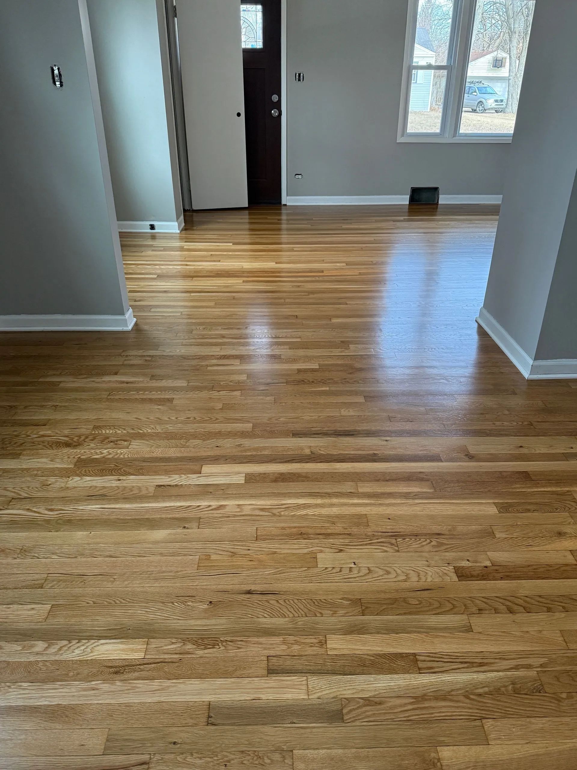 Empty room with hardwood floors, white walls, and windows letting in natural light.