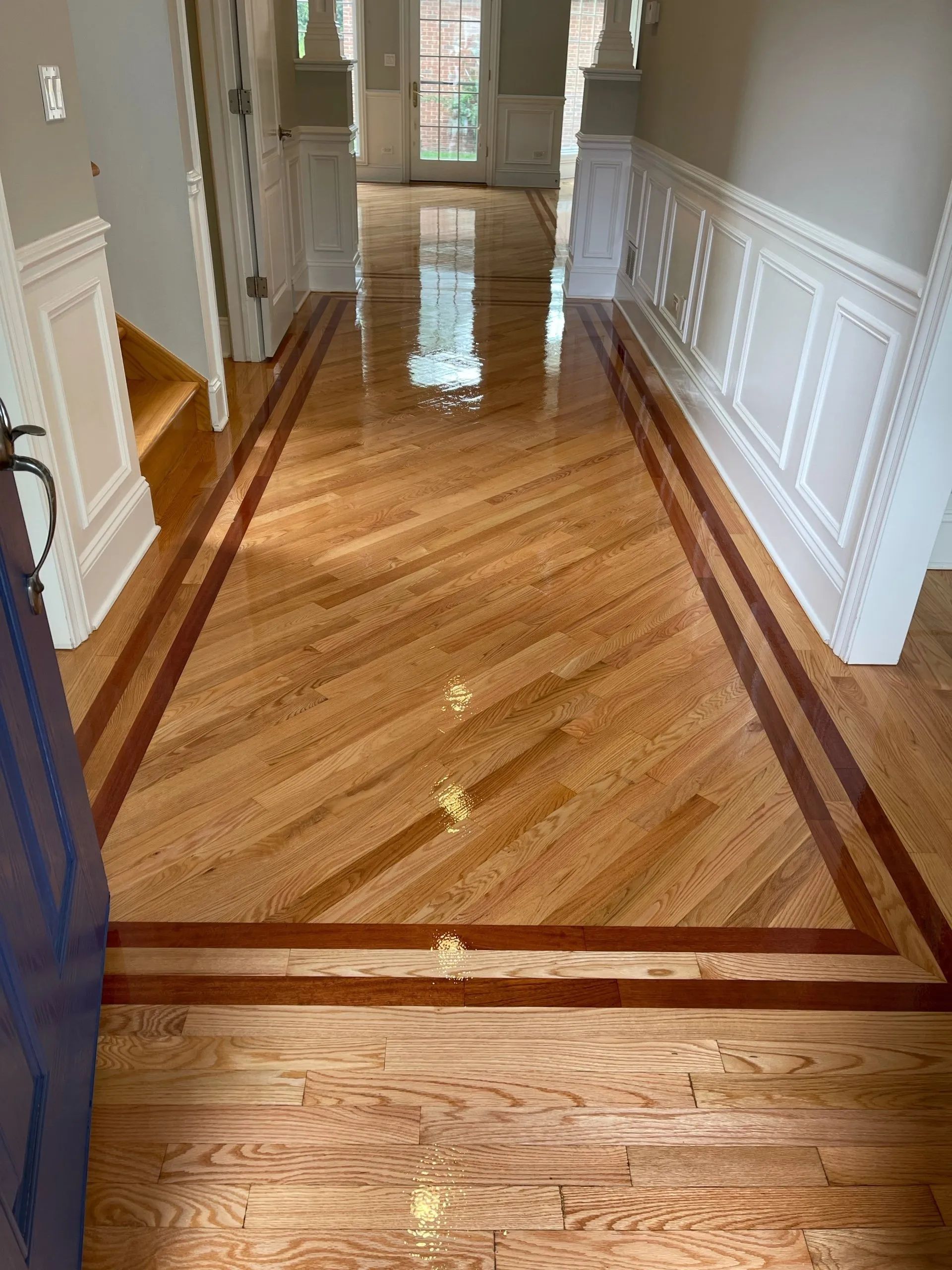 Hallway with hardwood floors, a herringbone pattern with a dark border, and white wainscoting.
