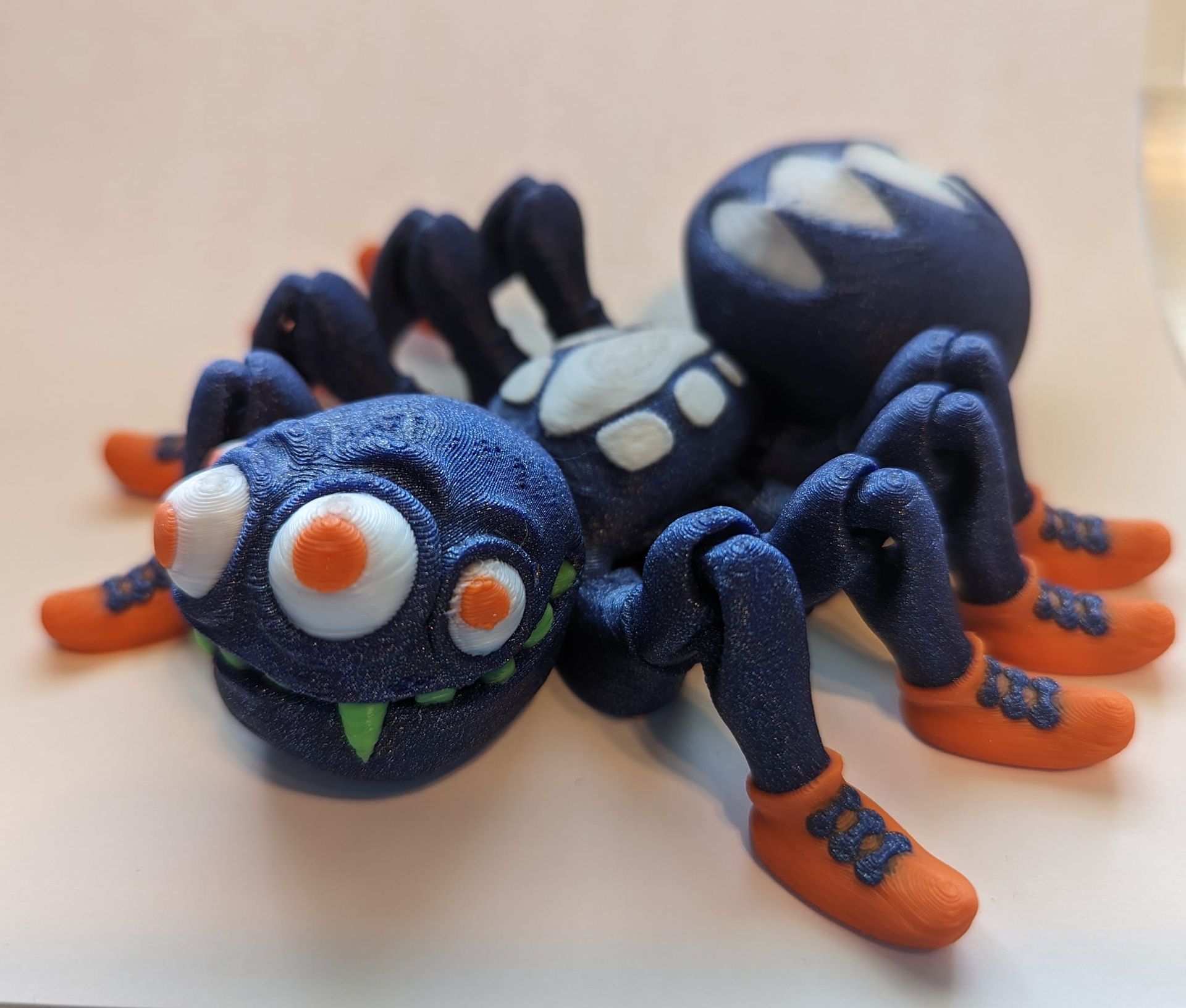 Blue-and-orange toy spider with big white eyes and a green fang on a light surface