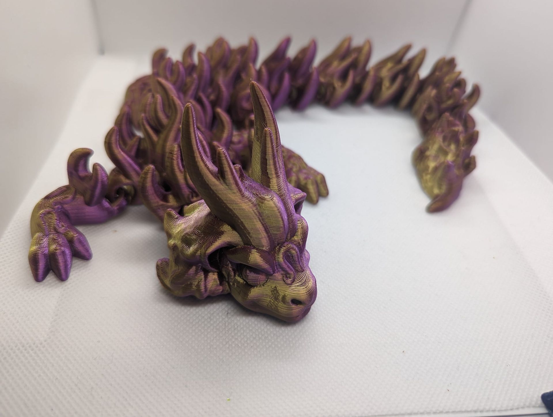 Purple and gold dragon figurine with a curled body on a white surface