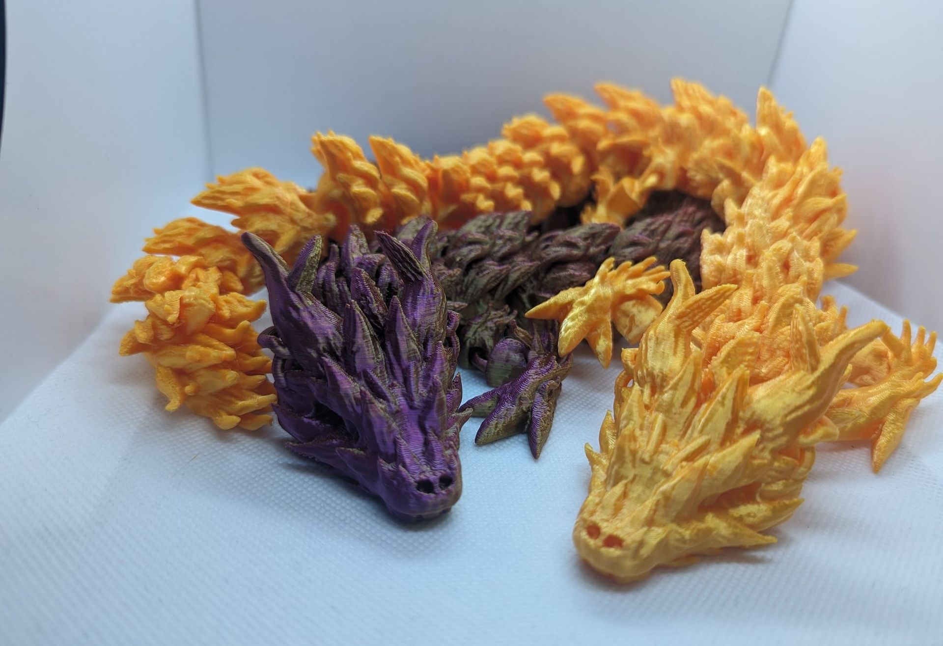 Three small dragon figurines in purple, yellow, and brown on a white surface