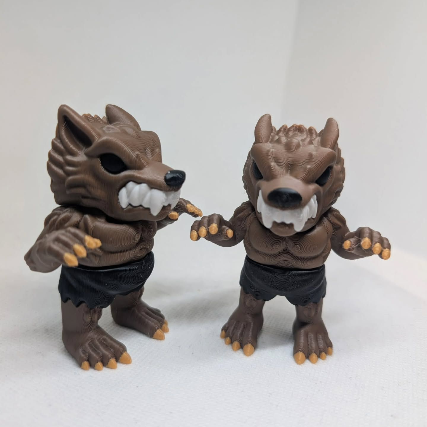 Two small wolf figurines wearing black shorts, posed on a white surface with arms outstretched.