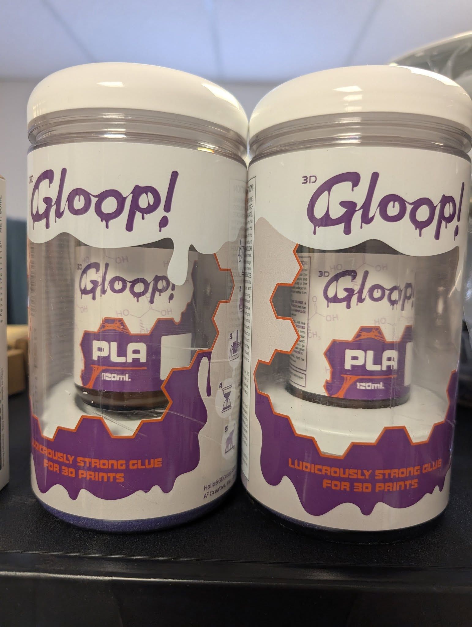 Two white Gloop! PLA filament bottles with purple labels on a dark surface