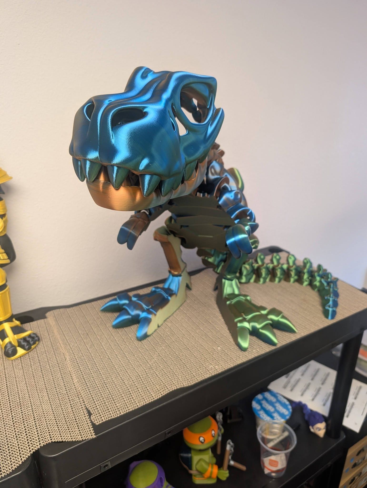 Blue-and-black toy dinosaur figure on a shelf, posed standing with open mouth and green tail accents.