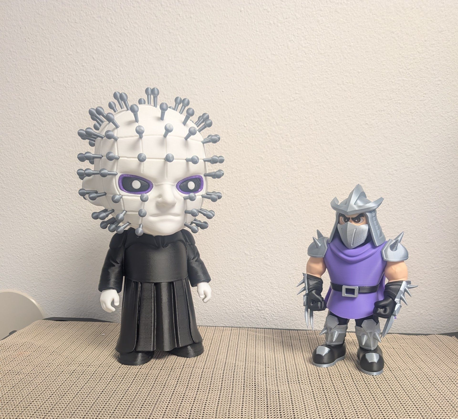 Two action figures on a woven surface: a white pinhead-style figure and a purple ninja figure.