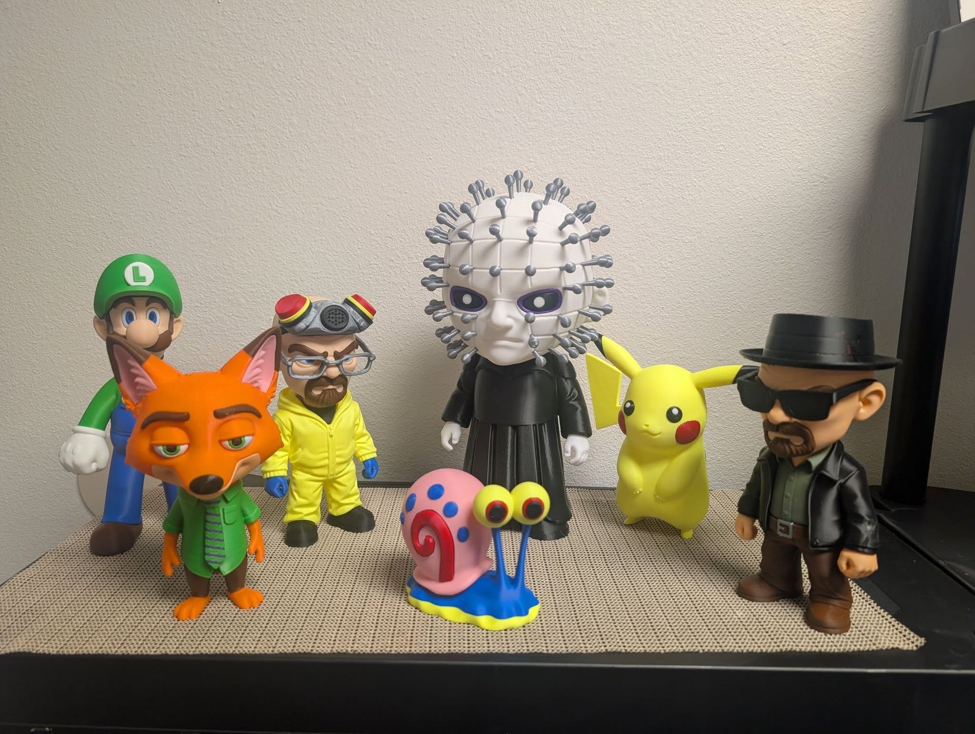 Toy figurines and characters lined up on a shelf, including Luigi, Pikachu, and a yellow snail in front.