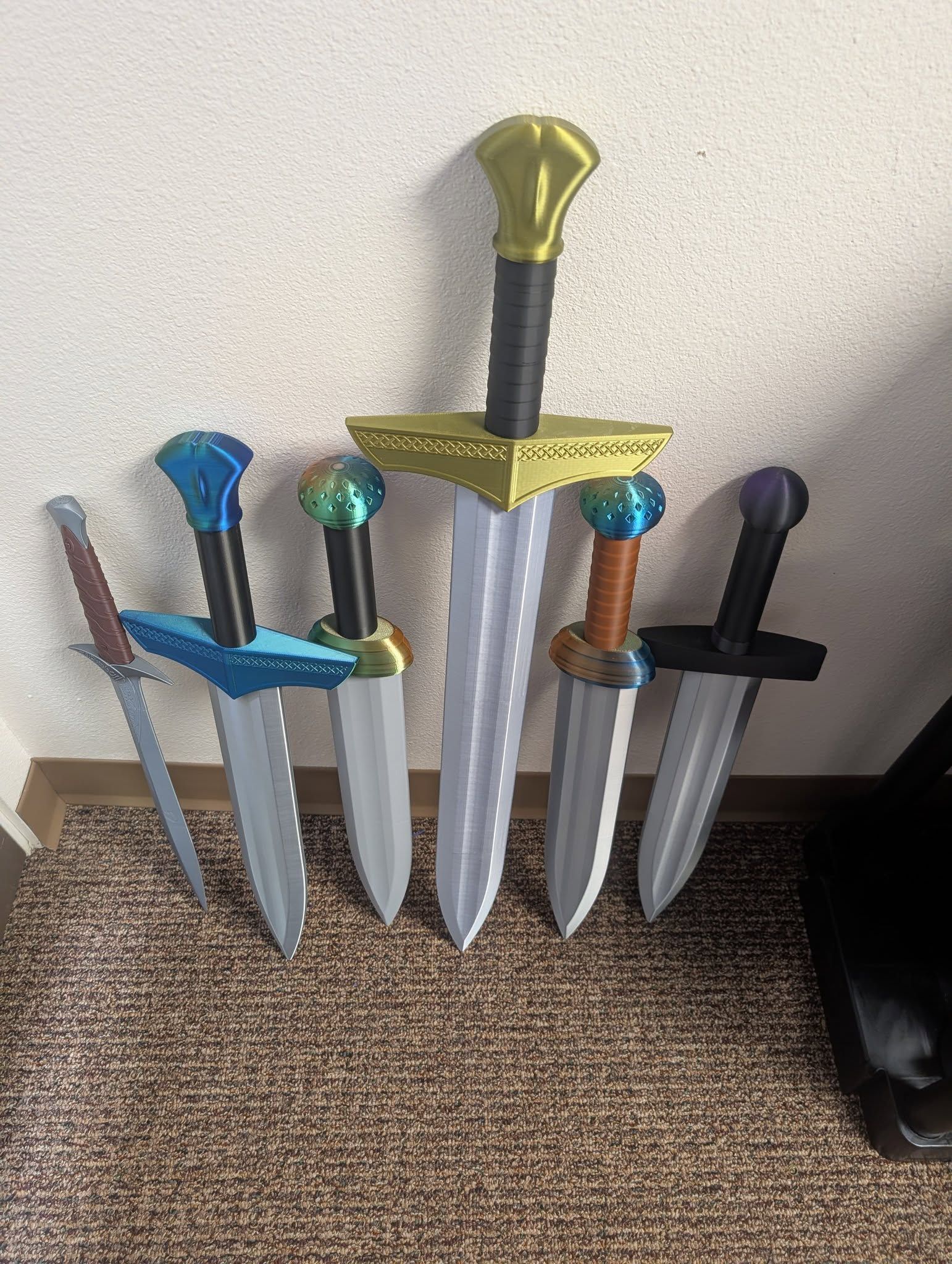 Several decorative sword props with colored hilts stand upright against a wall on a carpeted floor.