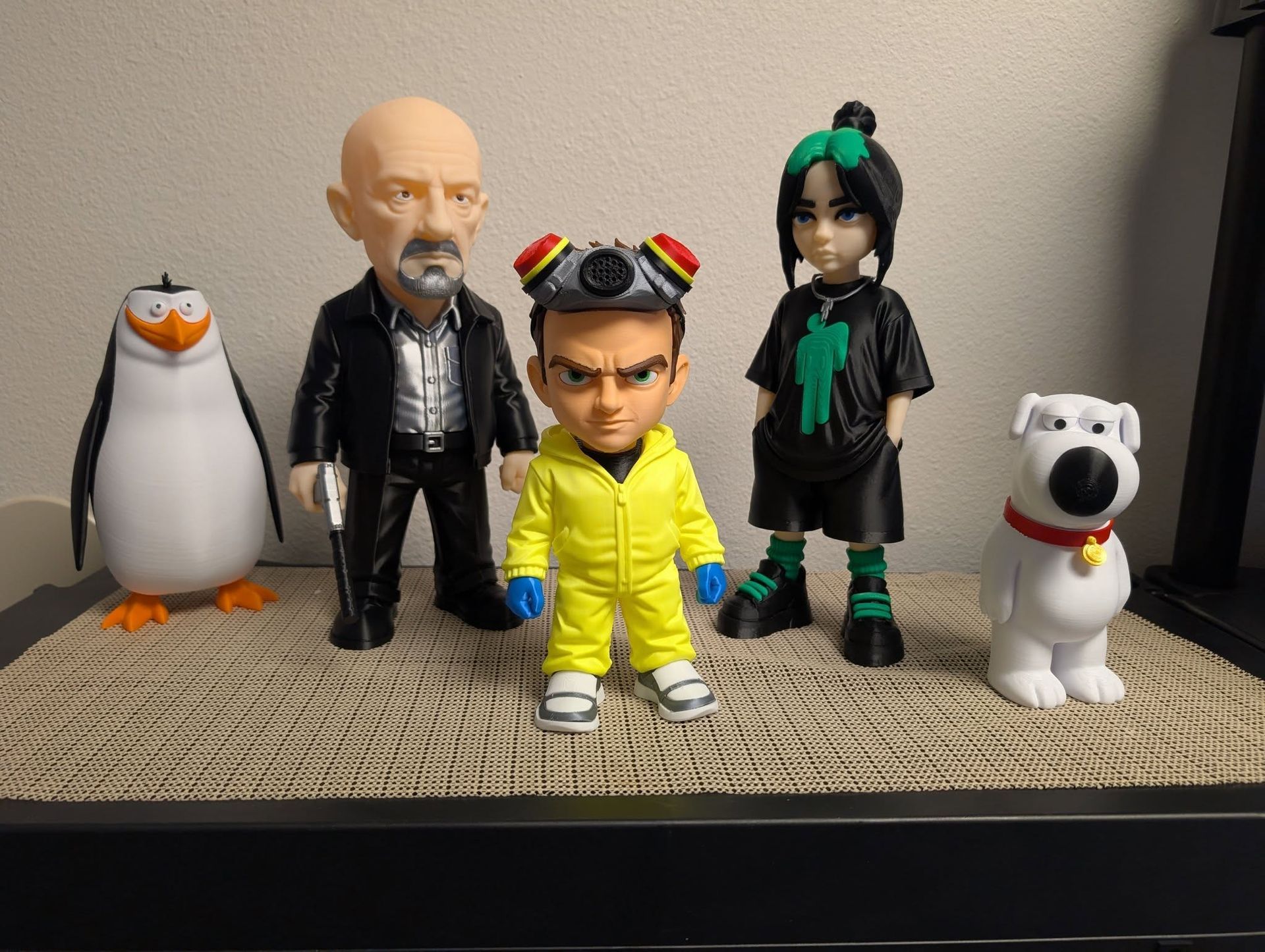 Five toy figures and a penguin figurine lined up on a woven surface against a beige wall.