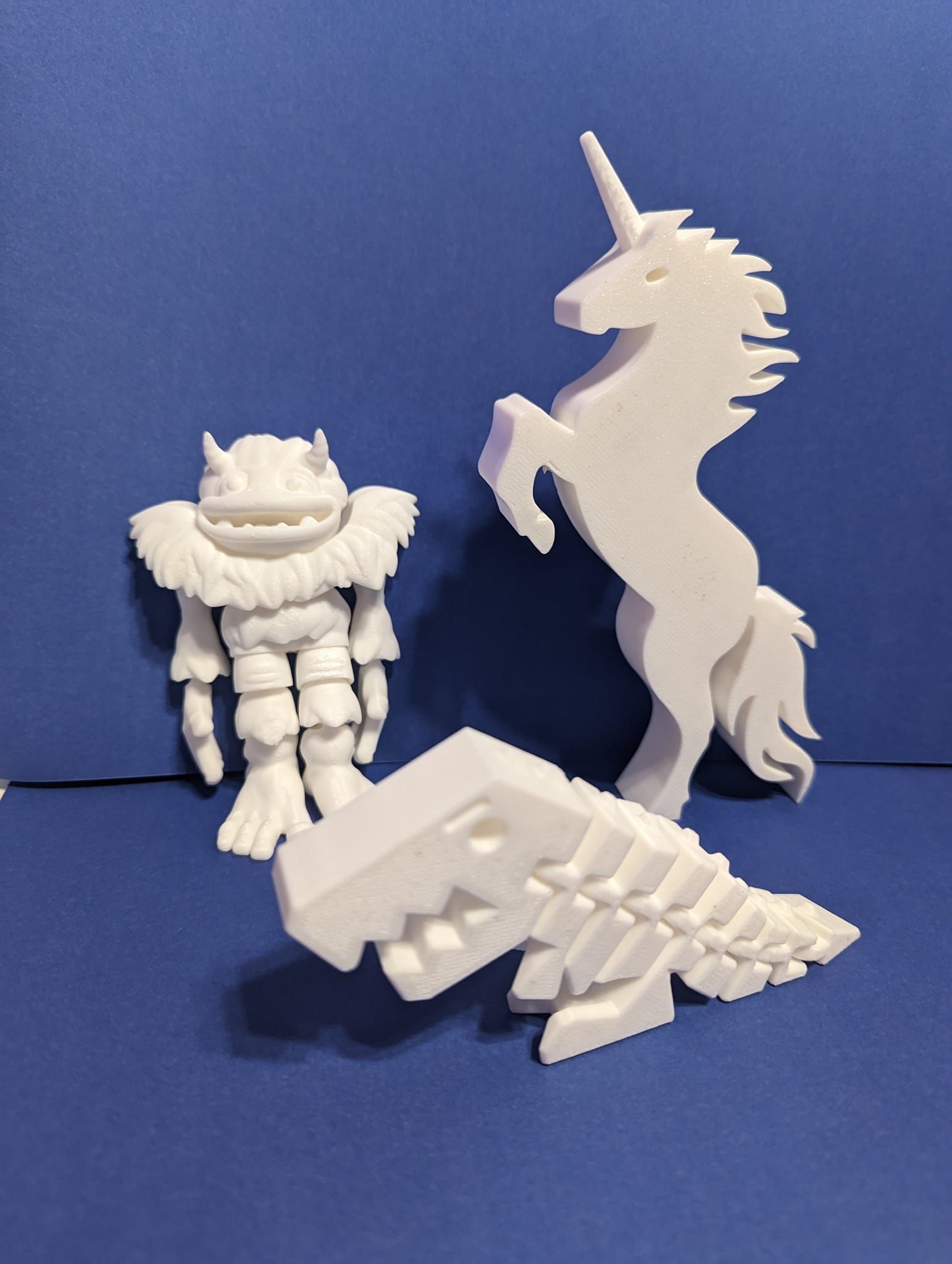 White 3D-printed figures: a unicorn, a squat armored character, and a dragon on a blue background