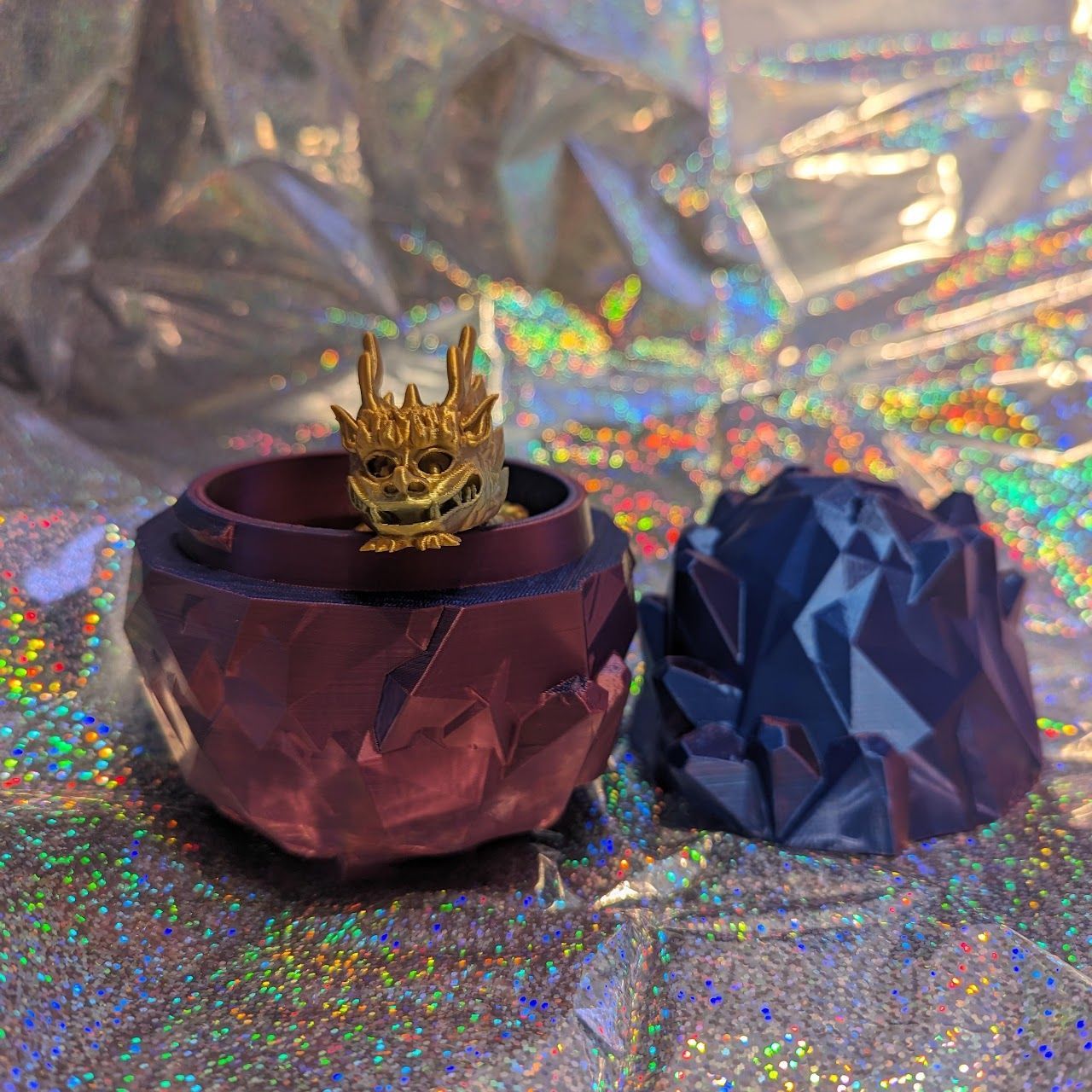 Purple jeweled candle holder with a gold crown on top beside a faceted blue ornament on glittery holographic fabric