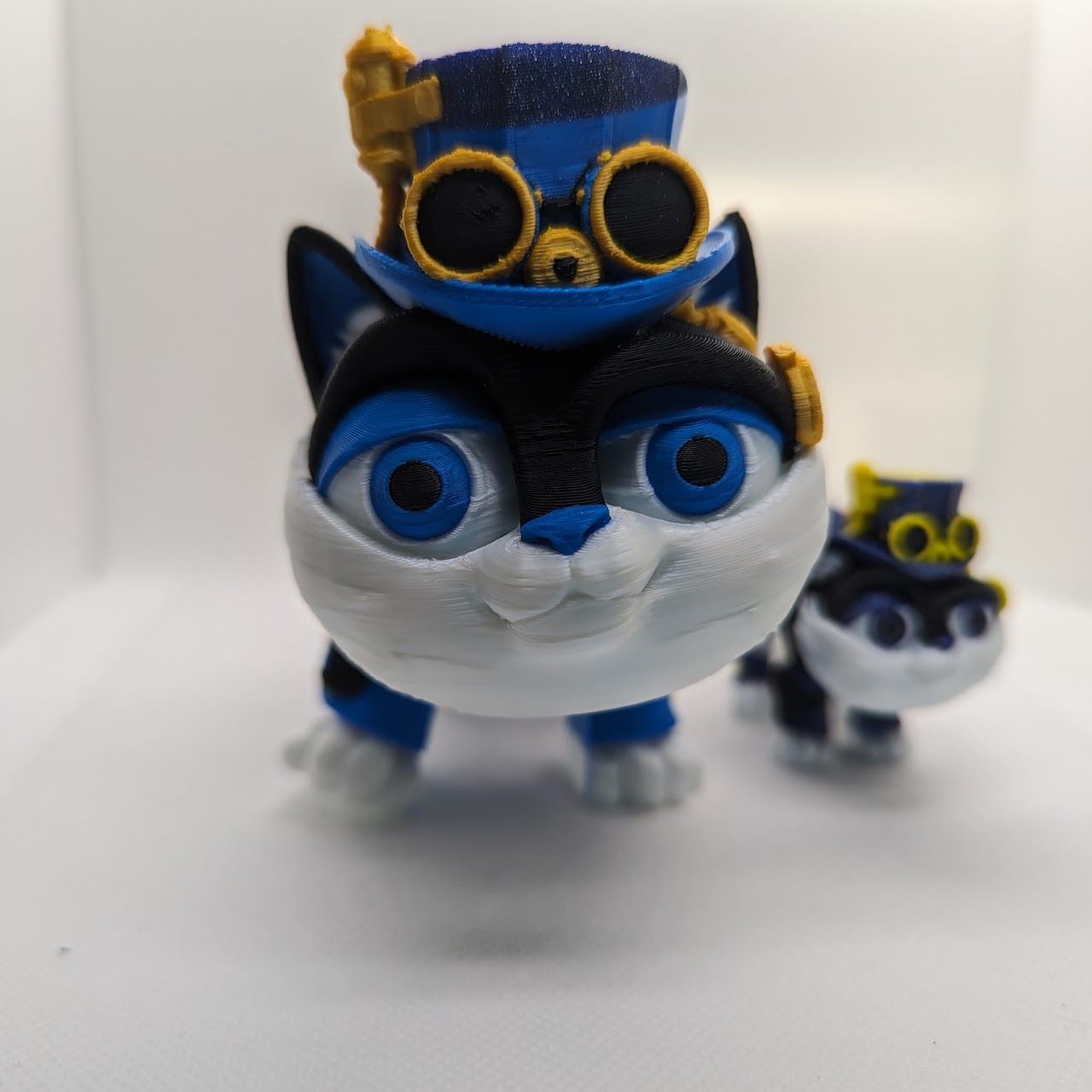Blue-and-white cat figurine with goggles and a tiny matching figure behind it on a white background