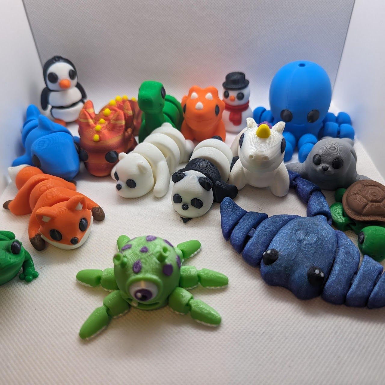 Assorted colorful clay animal figurines arranged on a white surface, including a penguin, spiders, and sea creatures