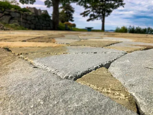 Close-up of stone pavement leading to a grassy area with trees and a distant ocean view.