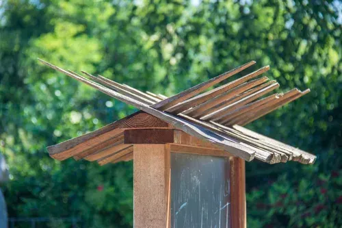 Wooden bird feeder roof with crossed slats, against a blurred green garden background