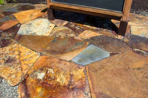 Rustic multicolored stone patio with a wooden bench base at the top edge