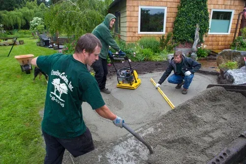 Workers pouring and leveling concrete in a backyard beside a house