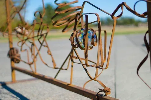 Rusty metal sculpture with abstract shapes on a roadside under a blue sky