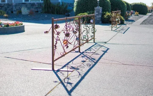 Metal garden trellis panels on a sunlit paved walkway, casting long shadows near landscaped hedges