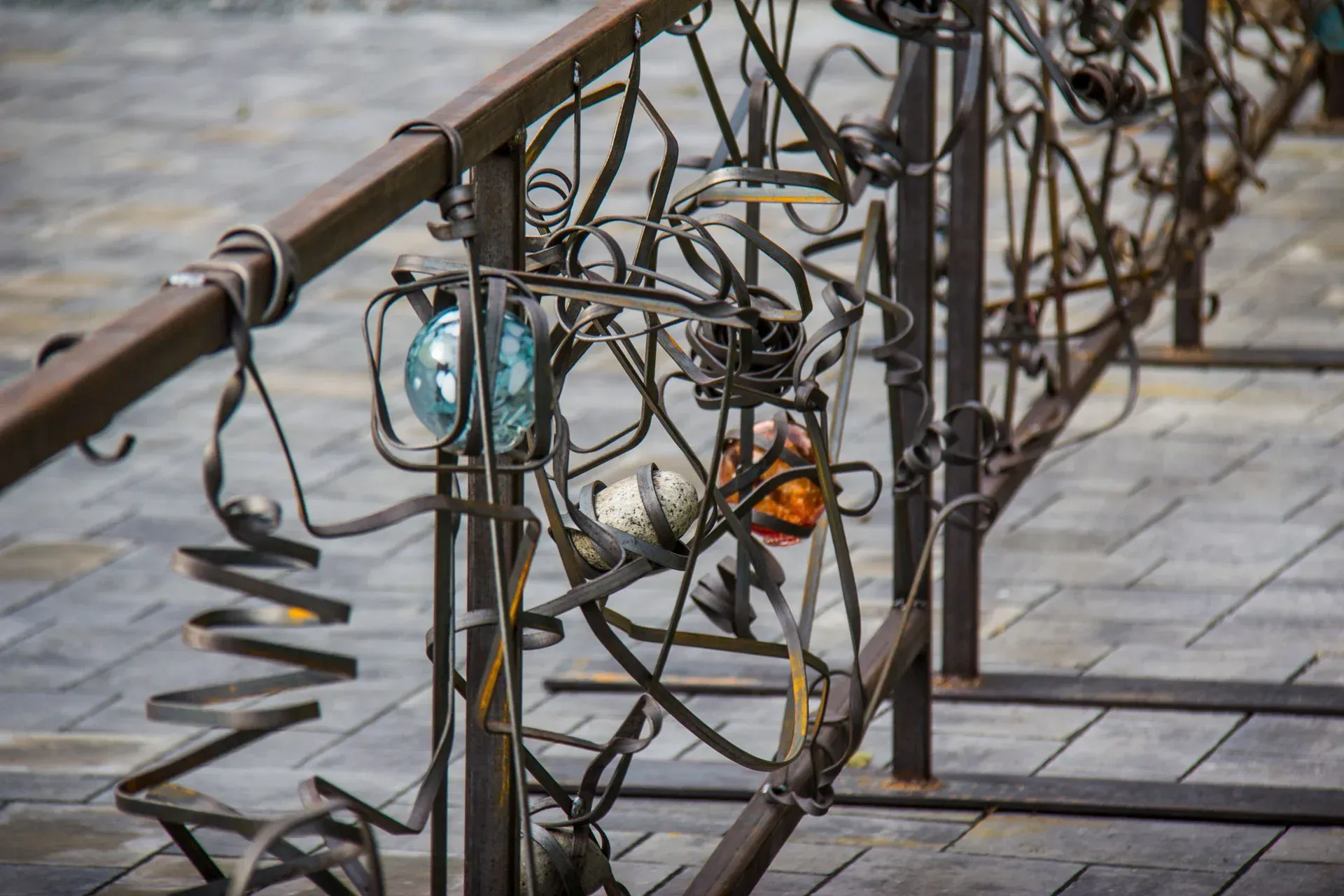 Rusty metal sculpture with tangled wire loops and hanging glass ornaments along a walkway