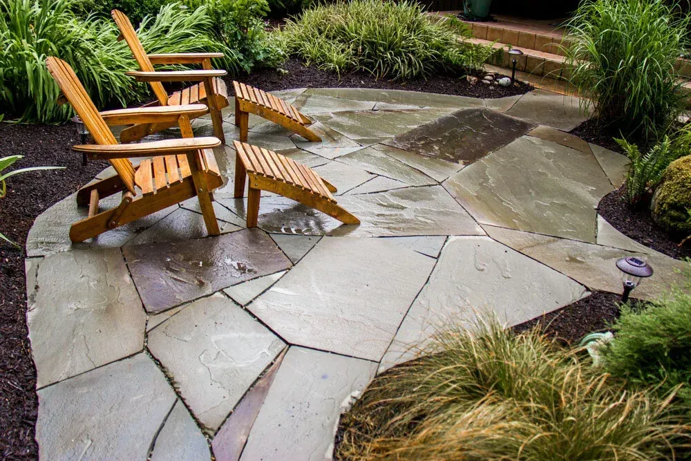 Wet stone patio with wooden Adirondack chairs and surrounding garden plants