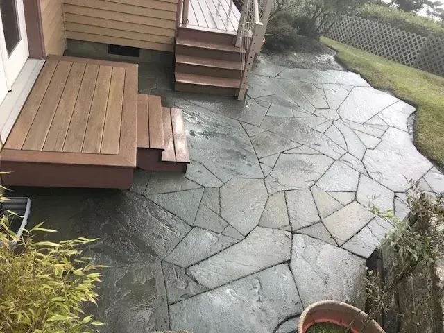 Rain-wet bluestone flagstone patio wrapping around cedar deck steps