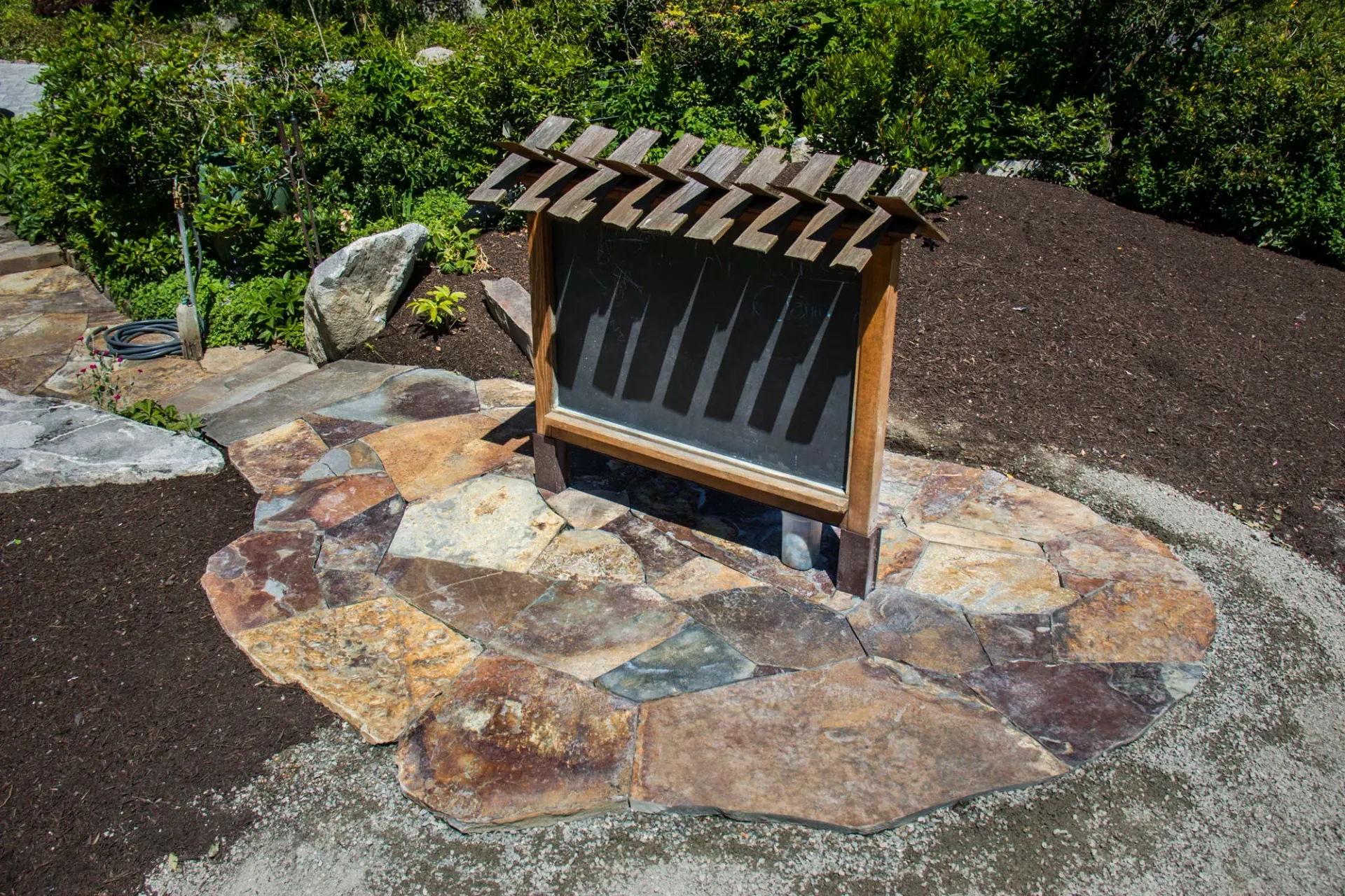 Wooden notice board on a stone path in a landscaped garden area