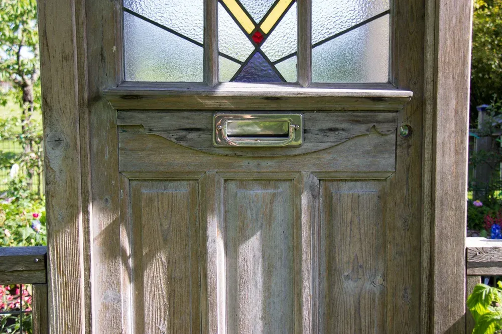 Wooden front door with stained-glass window and brass mail slot in sunlight