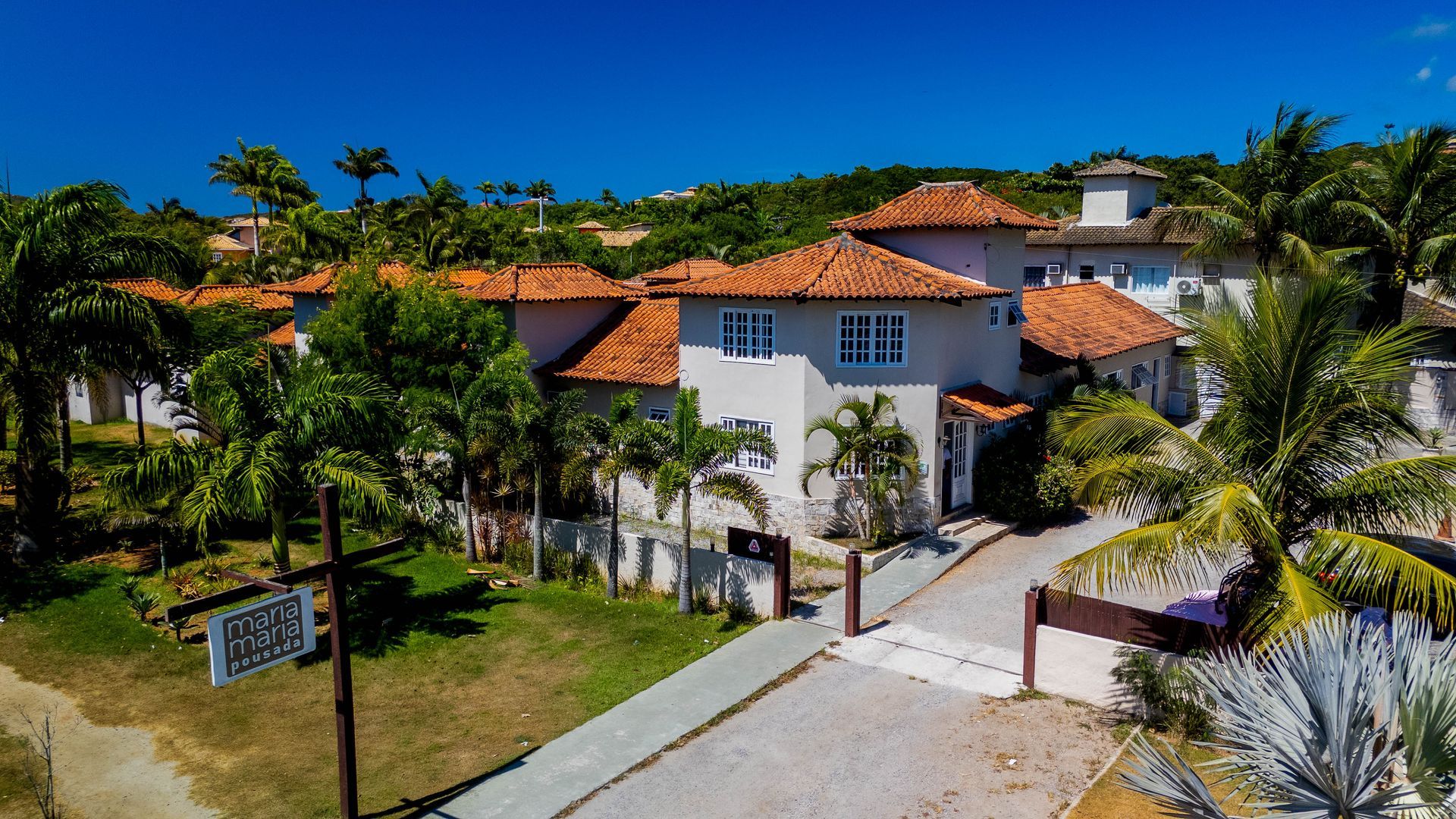 Grande edifício branco com telhado de telha laranja, palmeiras e céu azul.