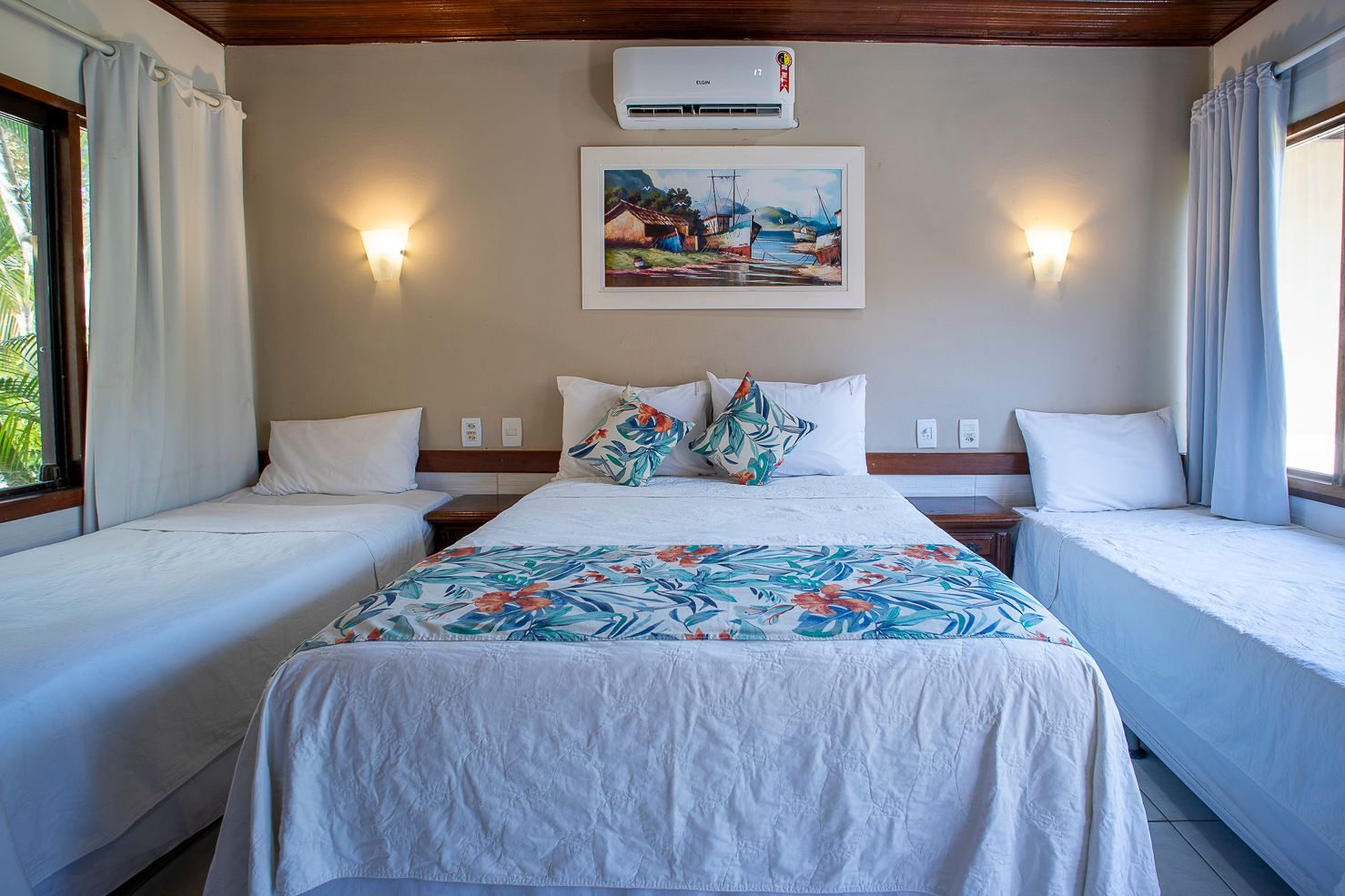 Quarto com uma cama de casal e duas camas de solteiro, decorado em tons claros e com uma colcha temática de praia.
