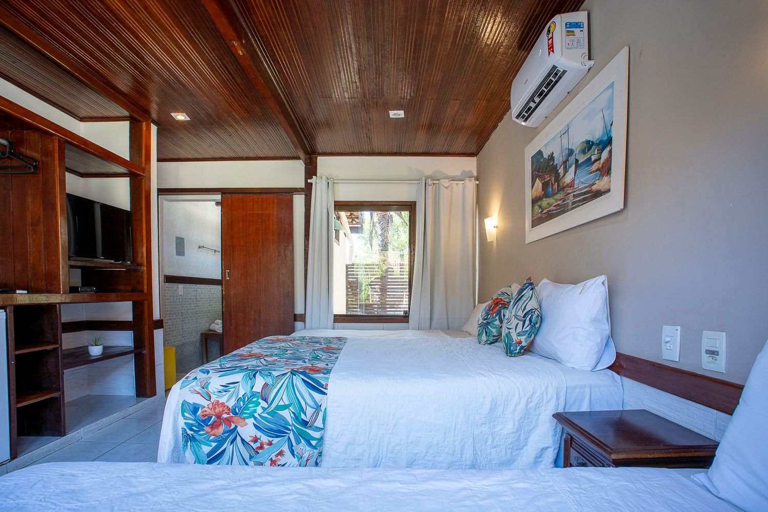 Quarto com cama de casal, detalhes florais, teto de madeira e obras de arte na parede.