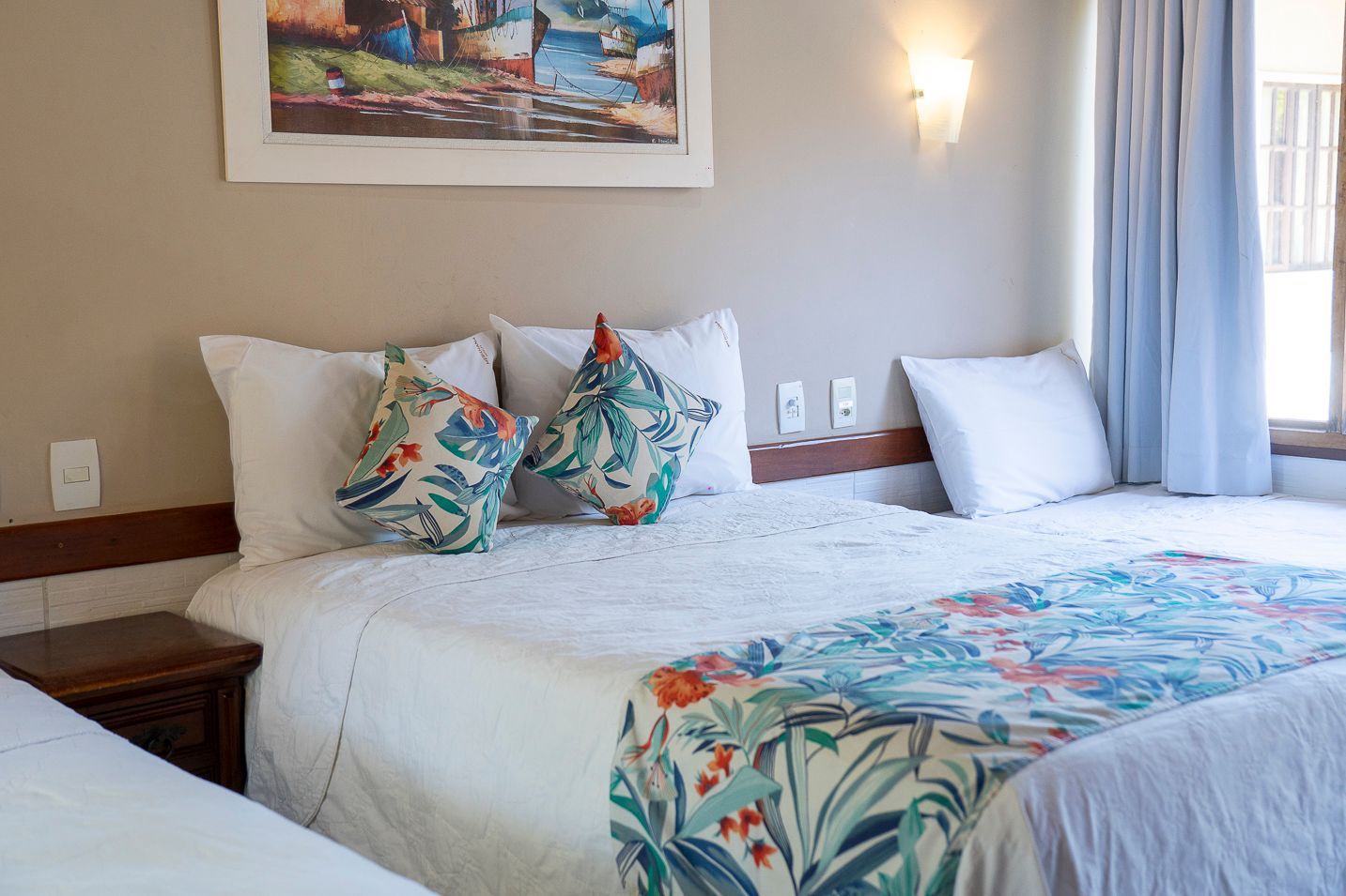 Quarto com uma cama de casal, uma cama de solteiro e almofadas coloridas. Um quadro está pendurado acima da cama.