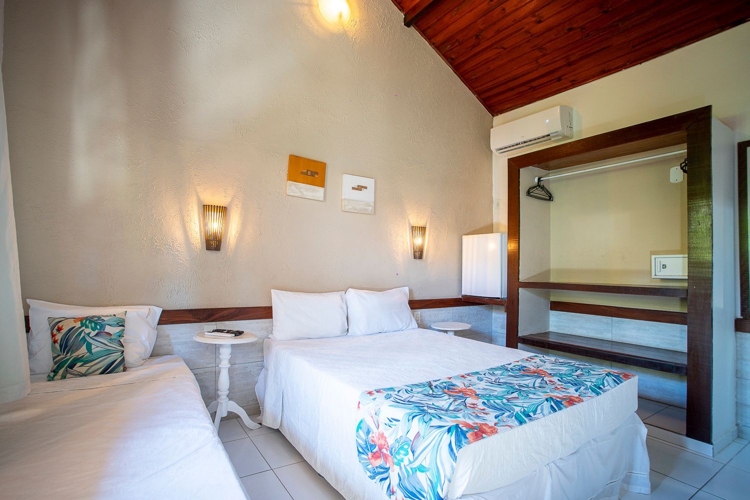 Quarto com paredes brancas, uma cama de casal com colcha floral azul e uma cama de solteiro.