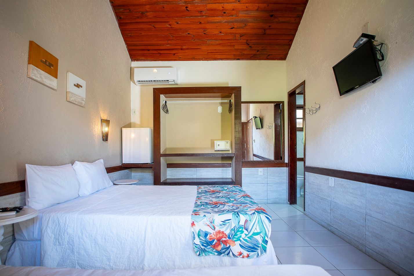 Quarto de hotel com cama, TV e teto de madeira.