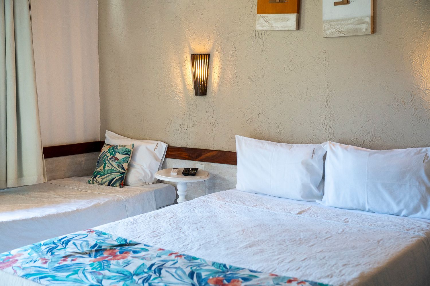 Quarto com cama de casal, cama de solteiro, obras de arte decorativas e aplique de parede.