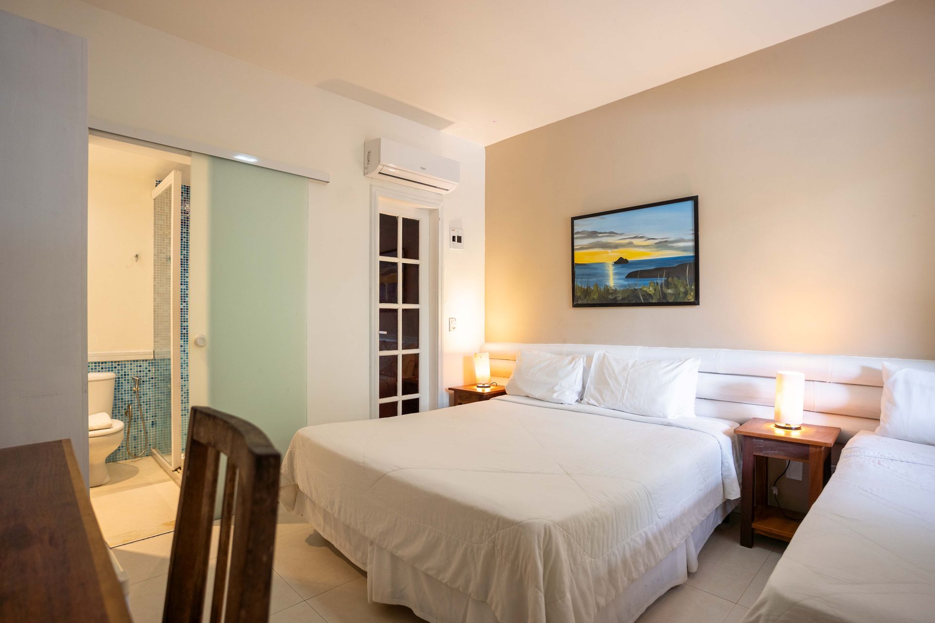 Quarto com uma cama de casal e uma cama de solteiro. Banheiro com porta de correr visível.