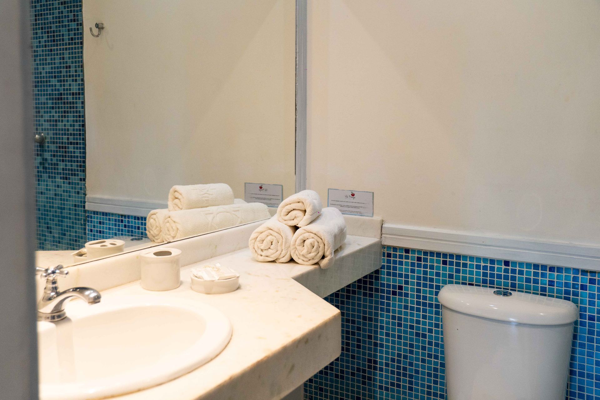 Banheiro com bancada branca, pia, toalhas e parede revestida com azulejos azuis.