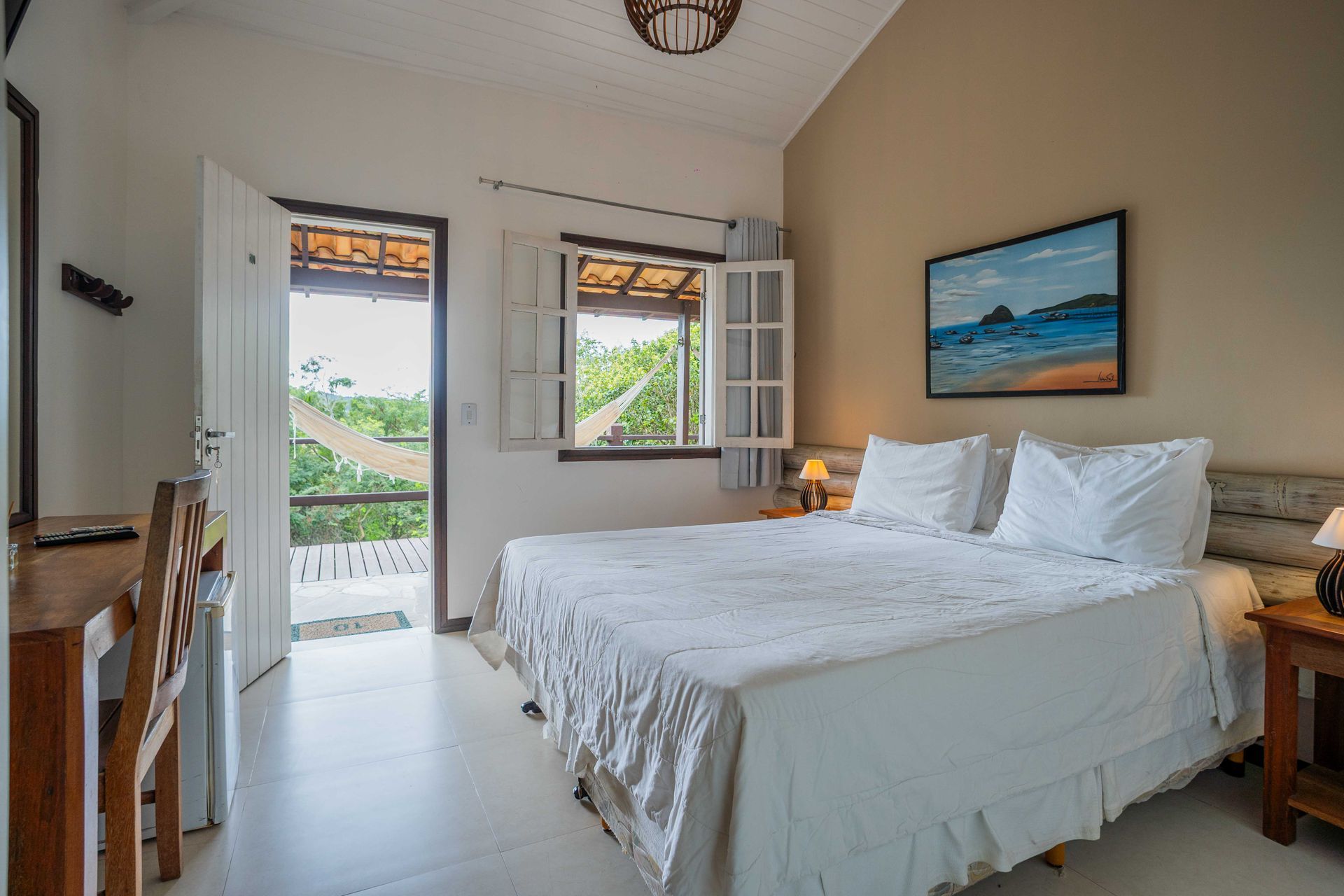 Quarto com cama king size, porta que dá para a varanda e pintura de paisagem.