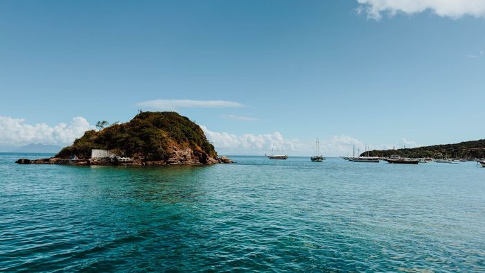 Ilha em um mar turquesa sob um céu azul claro, com barcos ao longe.