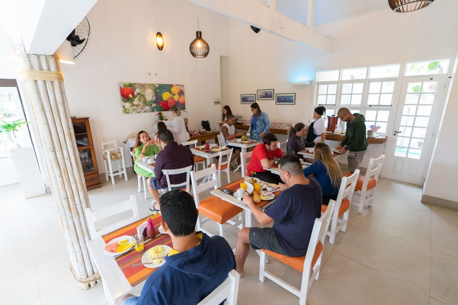 Pessoas comendo em mesas em um ambiente iluminado, provavelmente um café ou refeitório.