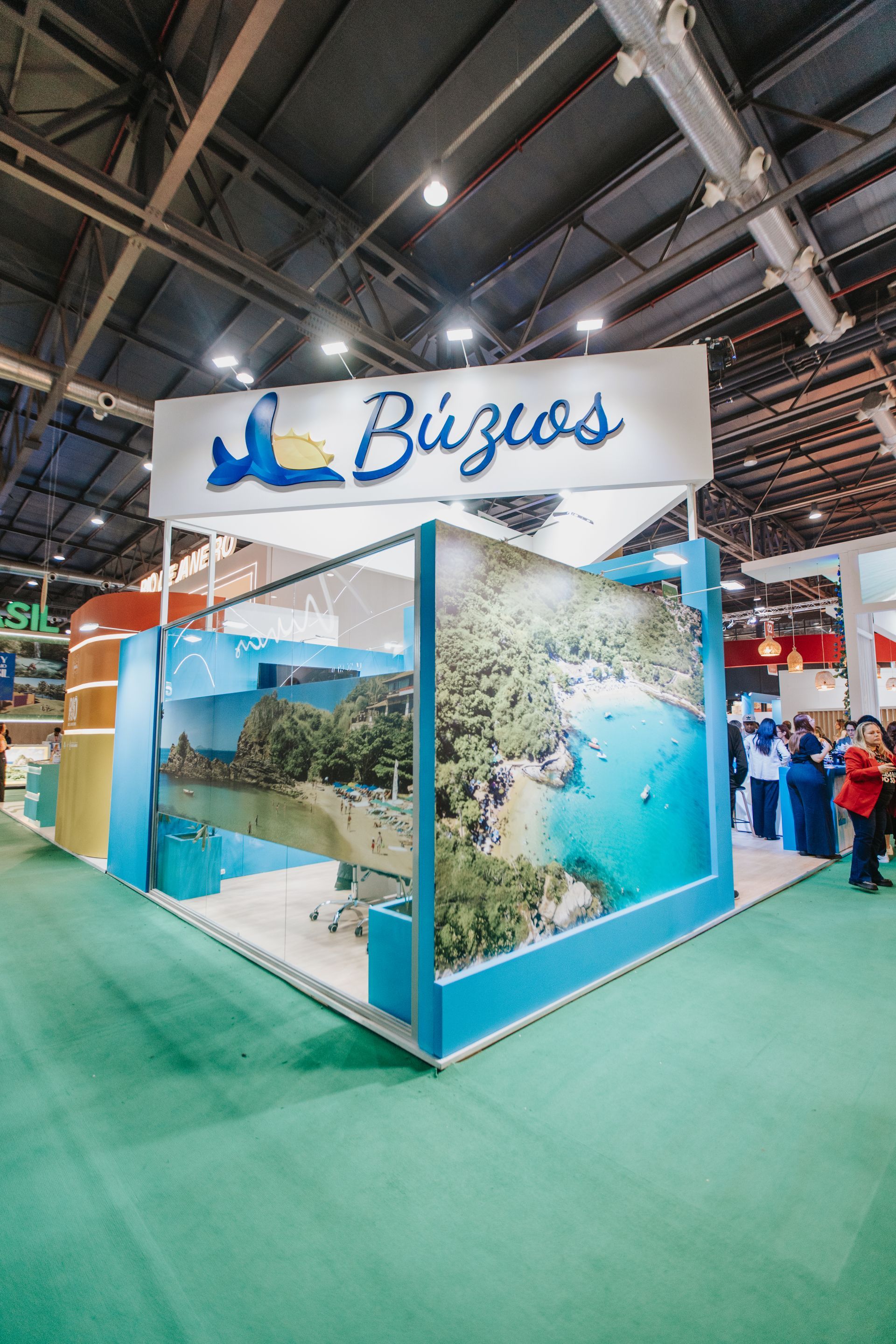 Estande turístico de Búzios em uma feira; design em azul e branco, grande foto de paisagem marítima, placa com o logotipo de um selo.