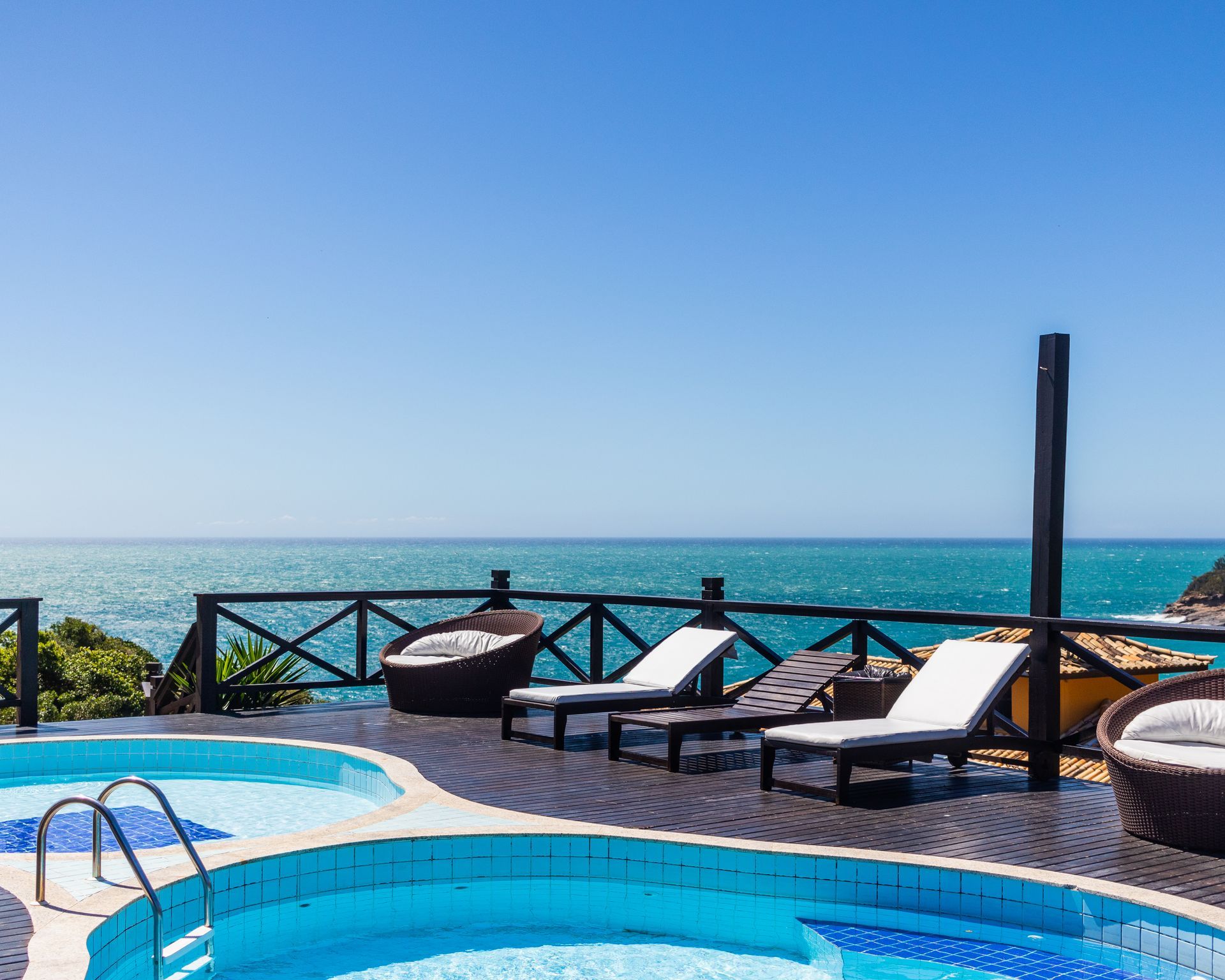 Área da piscina com vista para o oceano, com espreguiçadeiras, água azul e céu limpo.