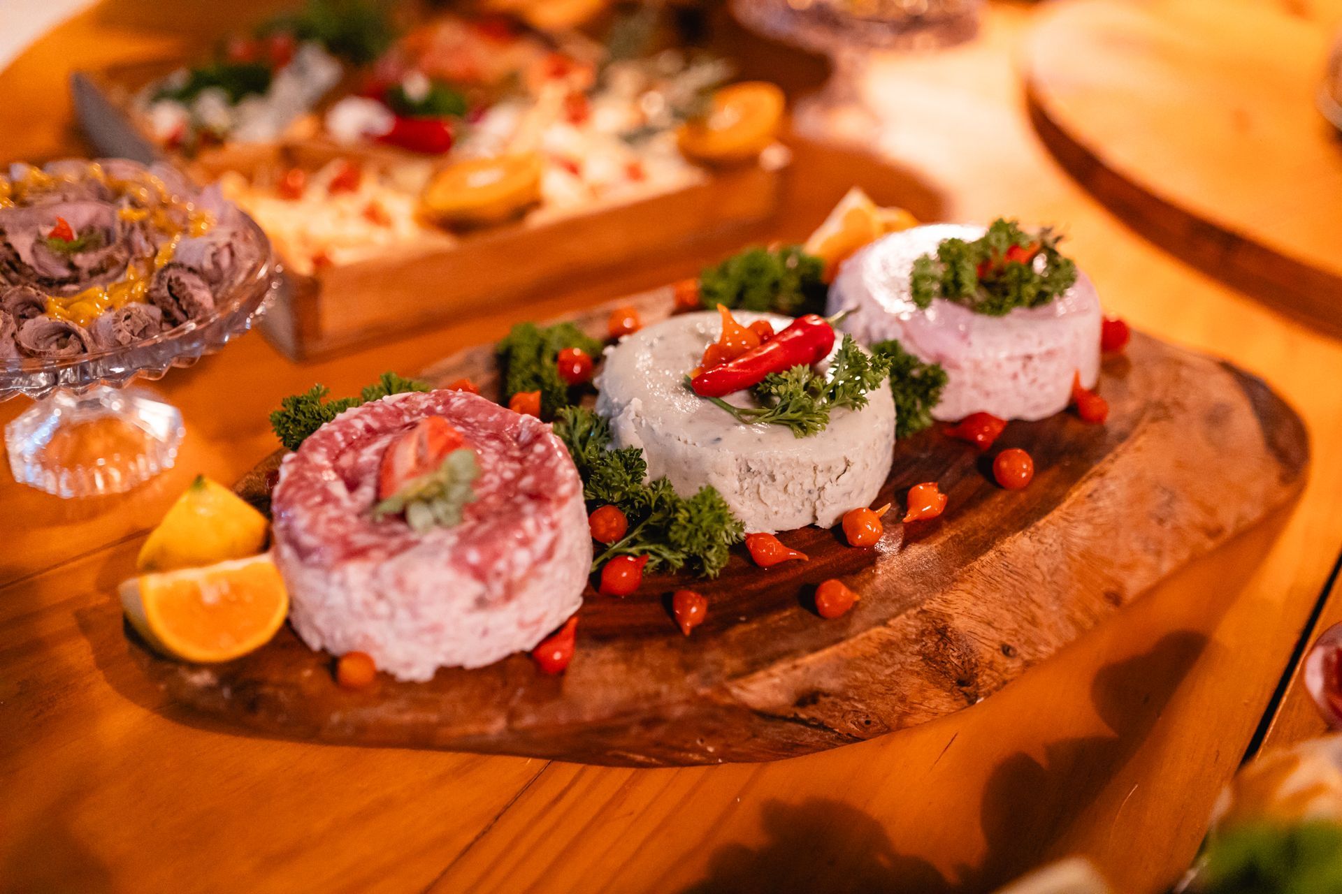 Colorful food display: various dips on a wooden platter, decorated with herbs, tomatoes and chili peppers.