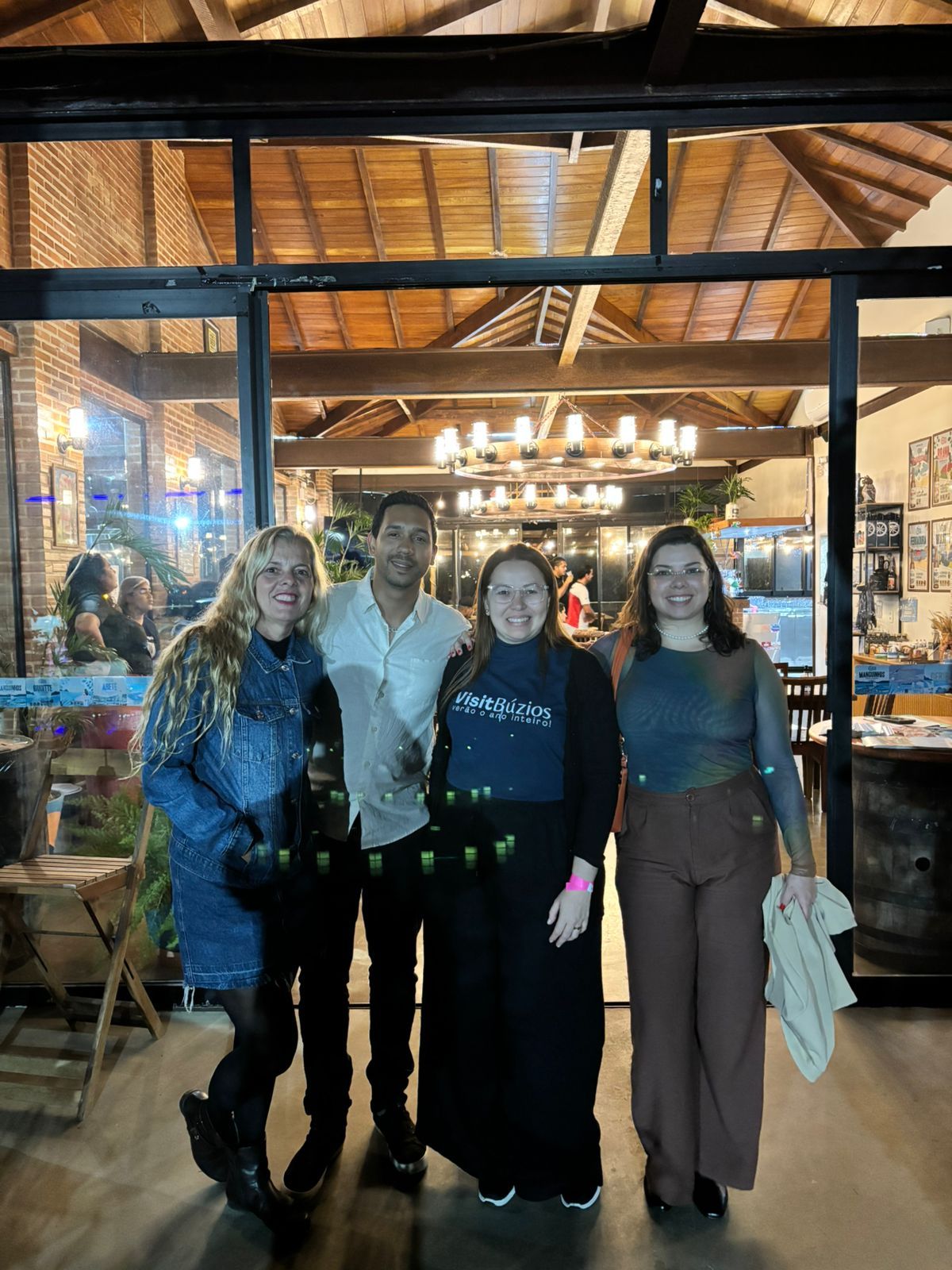 Quatro pessoas posam em frente a um edifício com paredes de vidro e iluminação aconchegante.