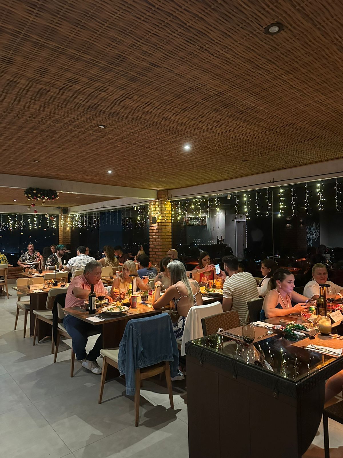 Interior de restaurante com clientes sentados às mesas, iluminação suspensa e teto de bambu.
