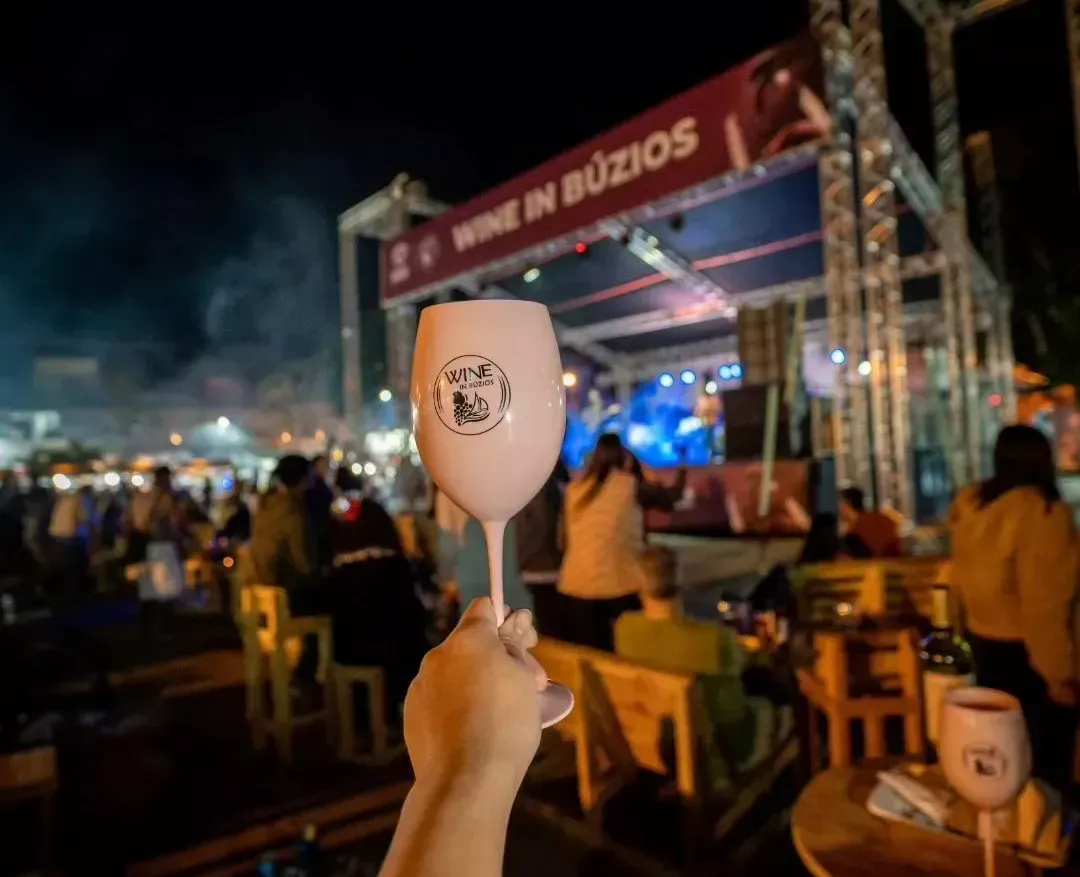 Uma mão segurando uma taça de vinho em um evento ao ar livre chamado