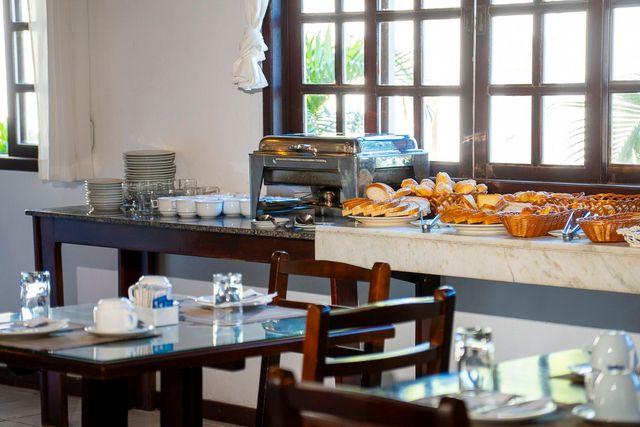 Mesa de buffet de café da manhã posta com comida e utensílios em frente a uma janela.
