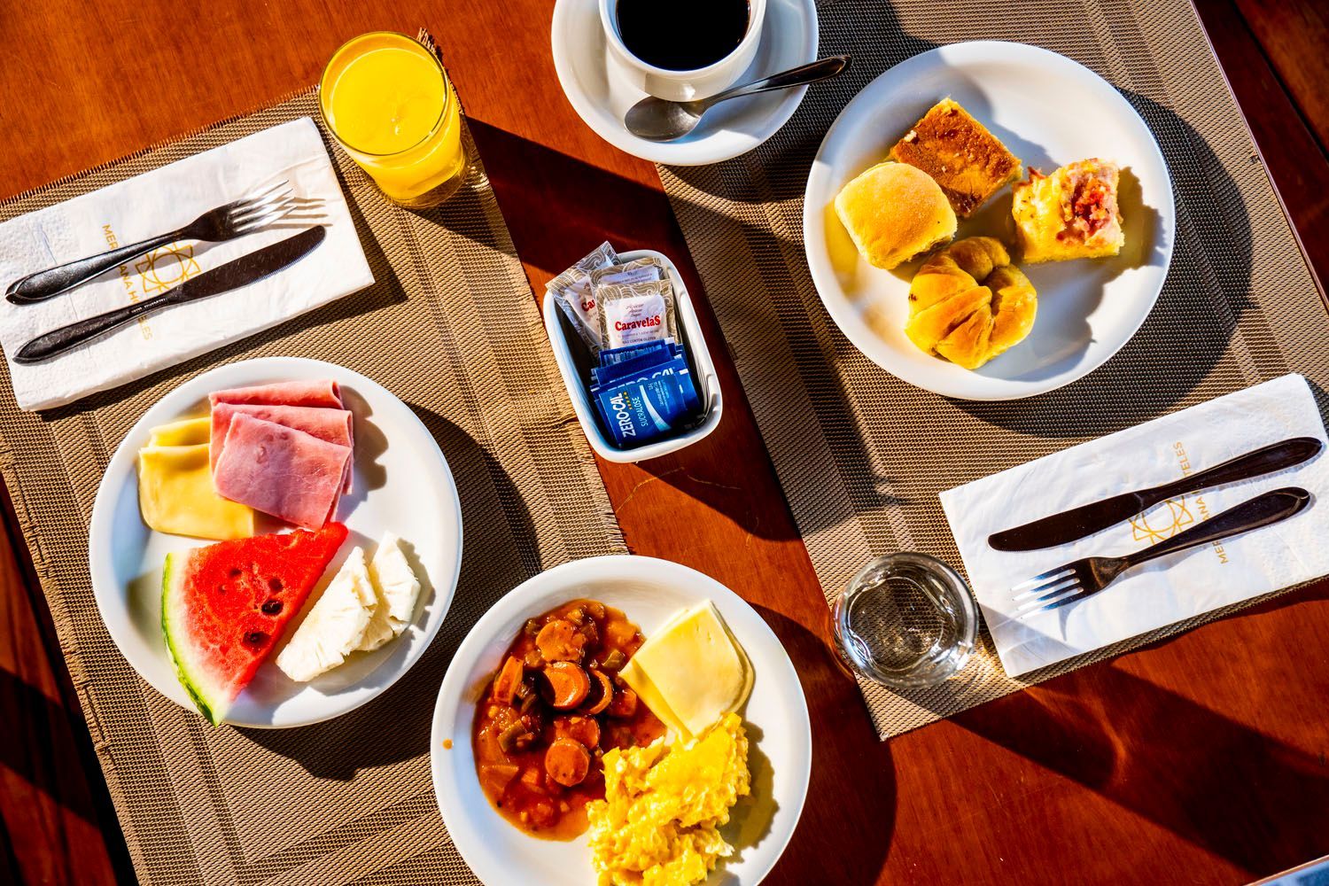 Mesa de café da manhã com pratos de comida, bebidas e talheres.