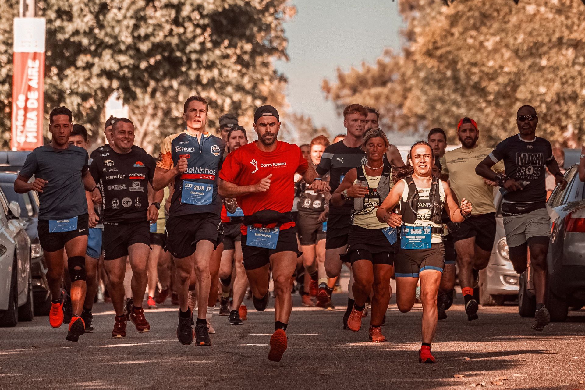Runners sprinting toward the finish line in a road race, with bibs and red shoes visible.